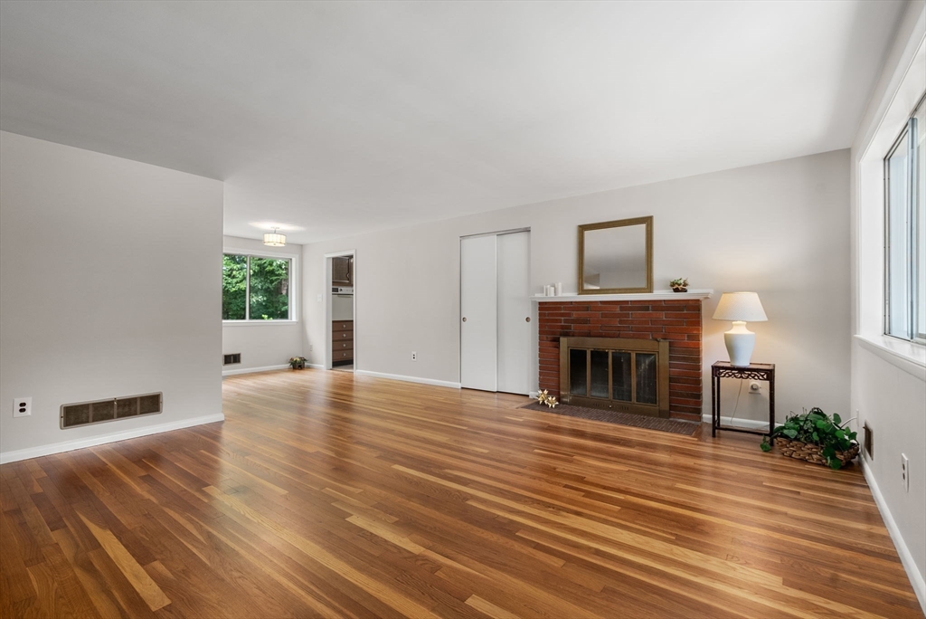 Living room with hardwood floors, a brick fireplace, and large windows.