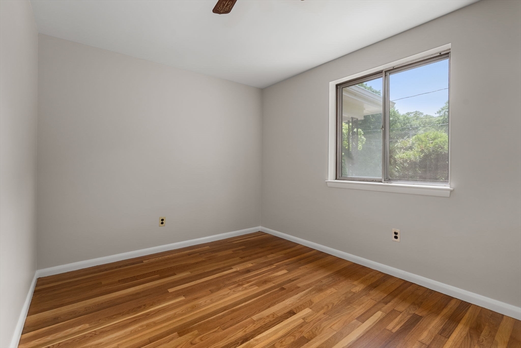 Empty room with hardwood floors, neutral walls, and a large window overlooking greenery.