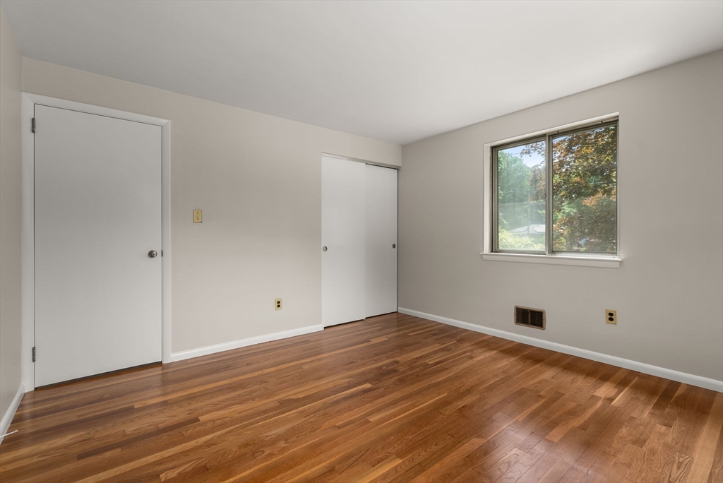 Empty bedroom with polished hardwood floors, a window overlooking trees, and a sliding closet door.