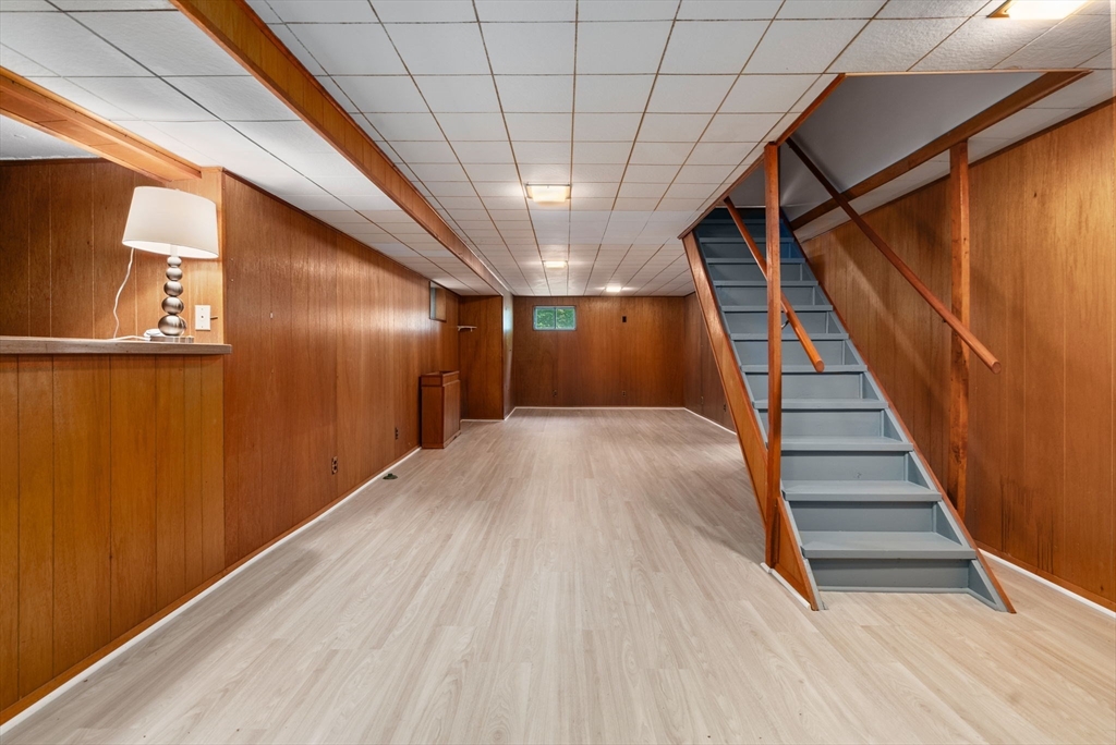 Basement room with wood-paneled walls, pale flooring, and a gray staircase.