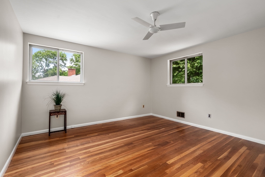 Mostly empty bedroom with warm hardwood floors, two windows, and a ceiling fan.