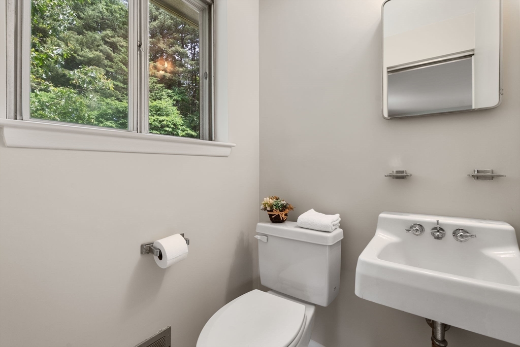 Bathroom with a wall-mounted sink and toilet beneath a window overlooking trees.