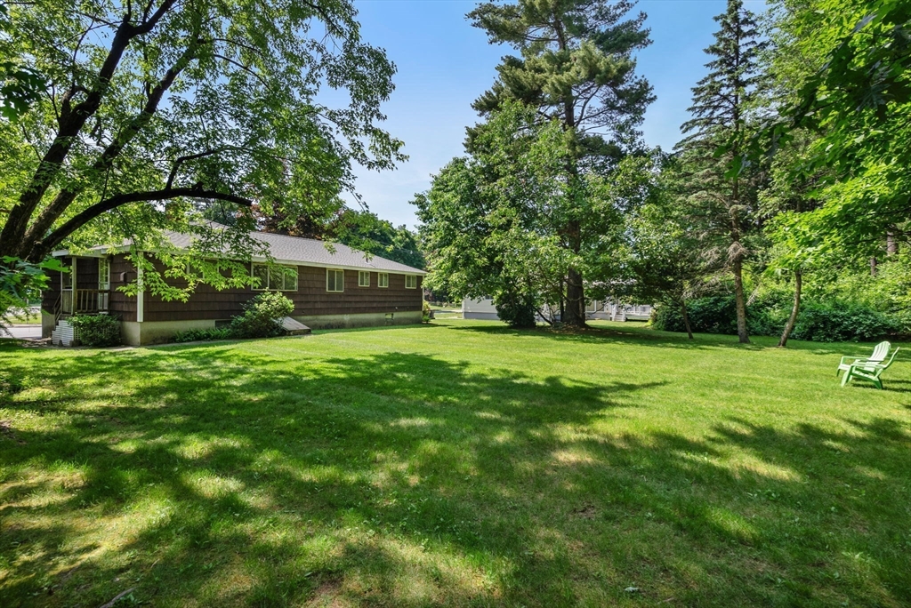 Single-story brown house beside a broad, tree-shaded lawn with a white chair.