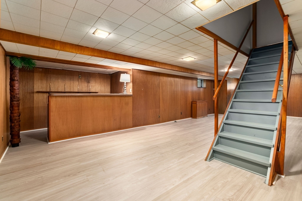 Basement with wood-paneled walls, a built-in bar counter, and gray stairs with wooden railings.