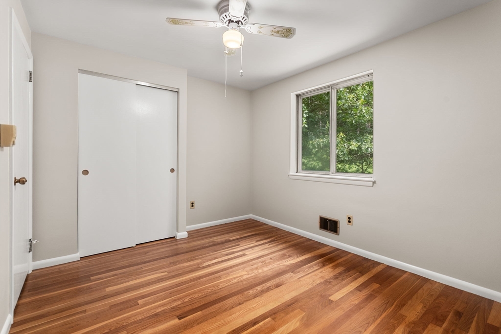 Vacant bedroom with polished hardwood floors, a sliding-door closet, and a ceiling fan.
