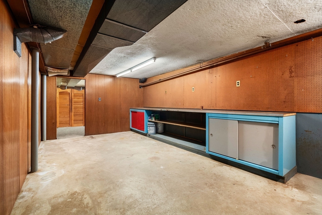Unfinished basement workshop with a blue built-in workbench, pegboard walls, and concrete floor.