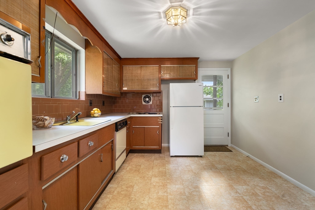 Kitchen with warm wood cabinets, brown tile backsplash, and a white refrigerator beside a glass-paneled door.