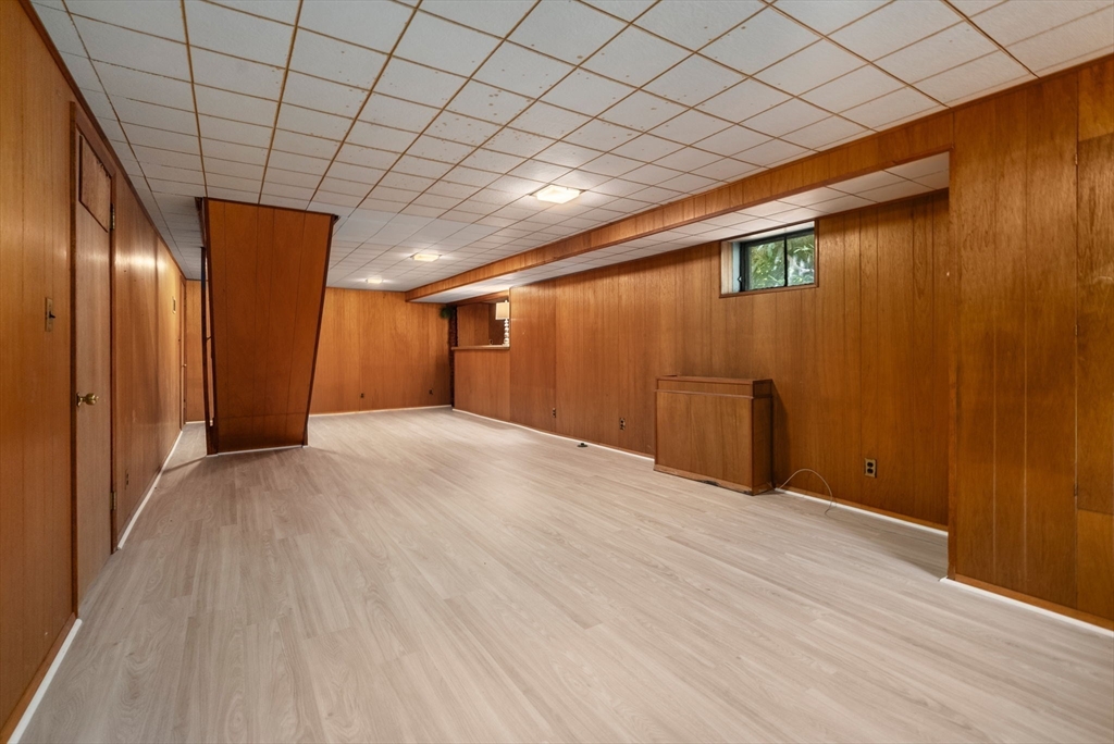 Finished basement with wood-paneled walls, pale flooring, and a small high window.
