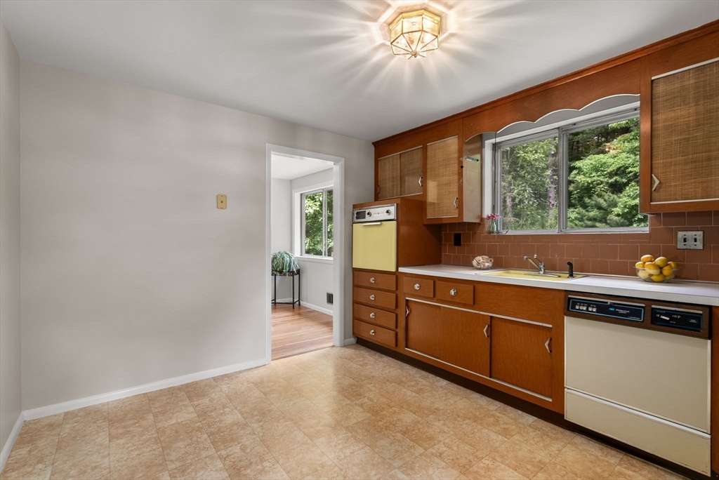 Kitchen with warm wood cabinets, a vintage yellow oven, and a wide window overlooking greenery.
