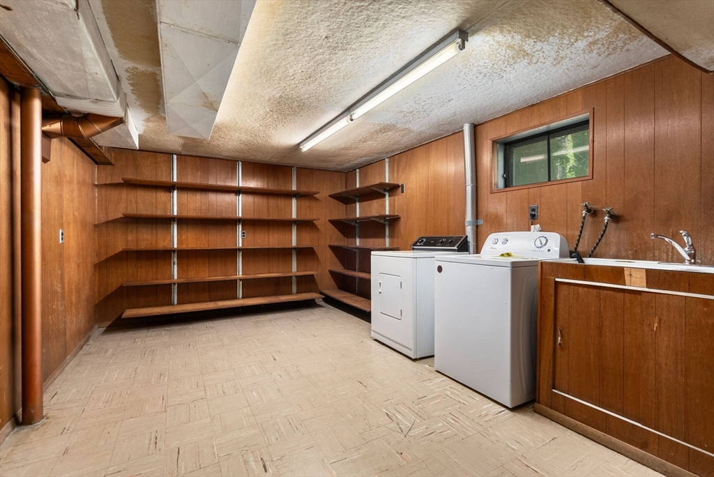 Laundry room with wood paneling, a washer and dryer, and wall-length open shelving.