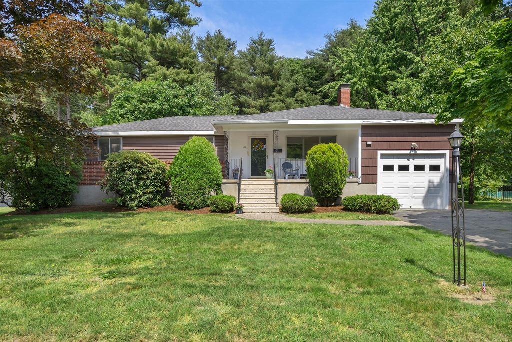 Single-story home with a covered porch, white garage door, and mature trees.