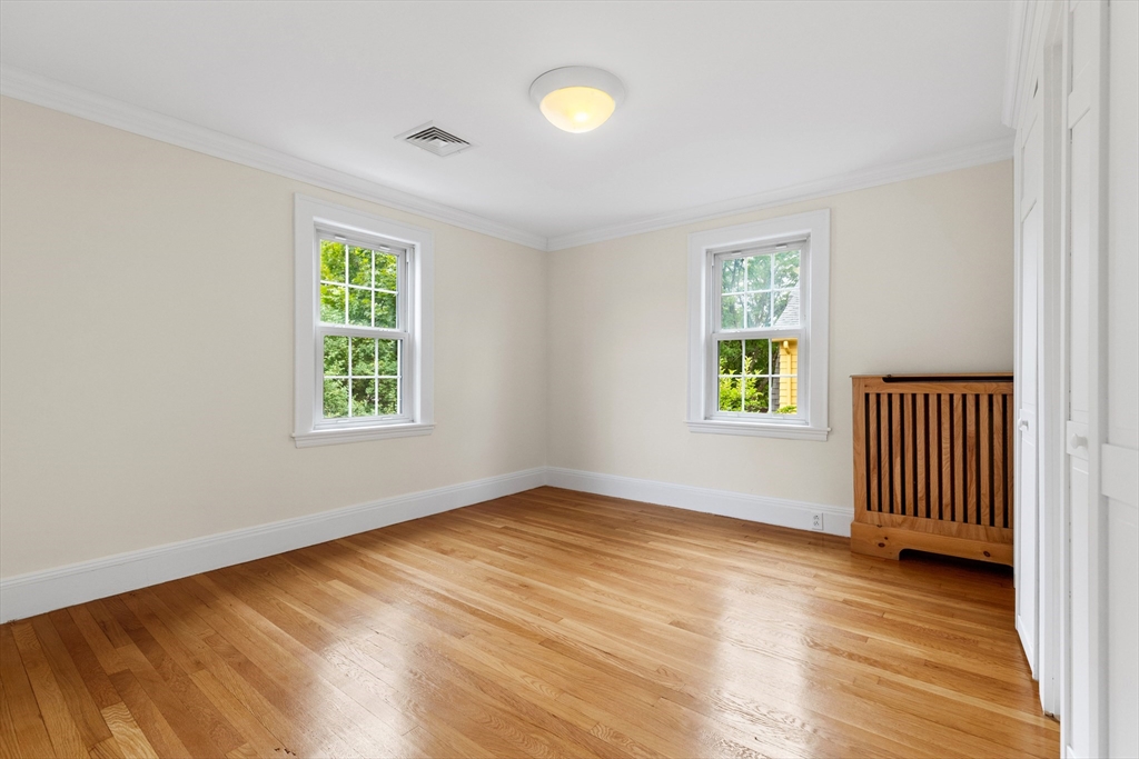 Empty bedroom with hardwood floors, two windows, and a wooden radiator cover.