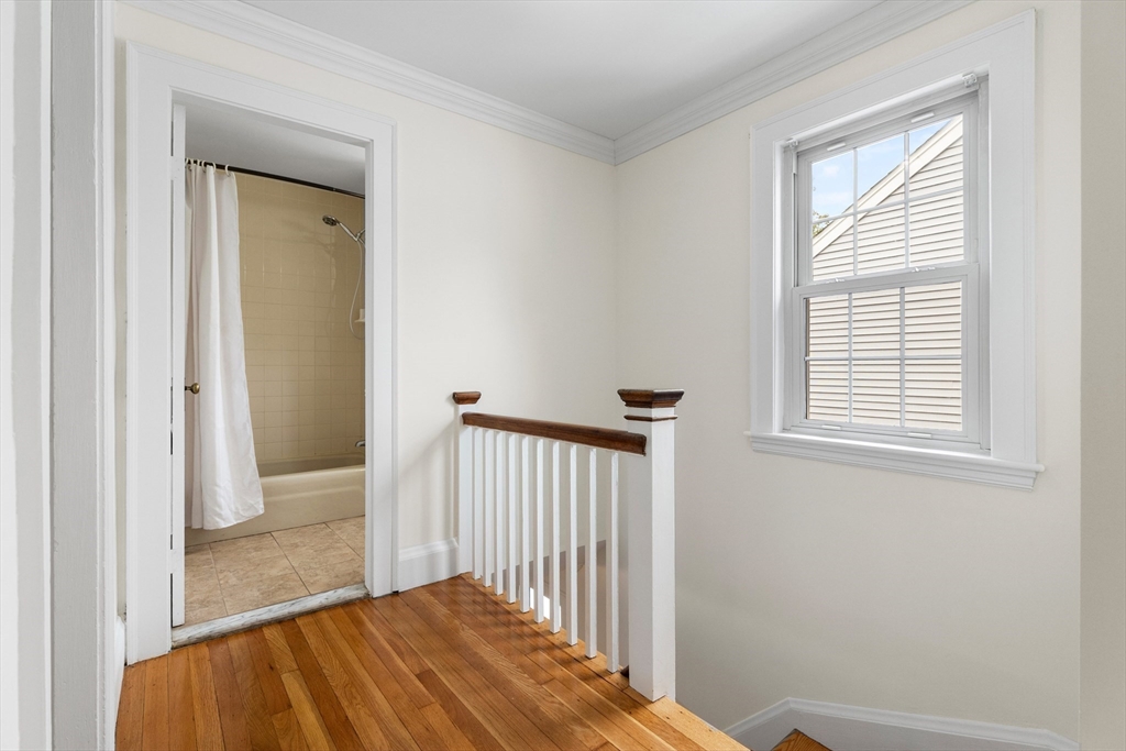 Upstairs landing with hardwood floors and a wood-capped railing beside an open bathroom doorway.