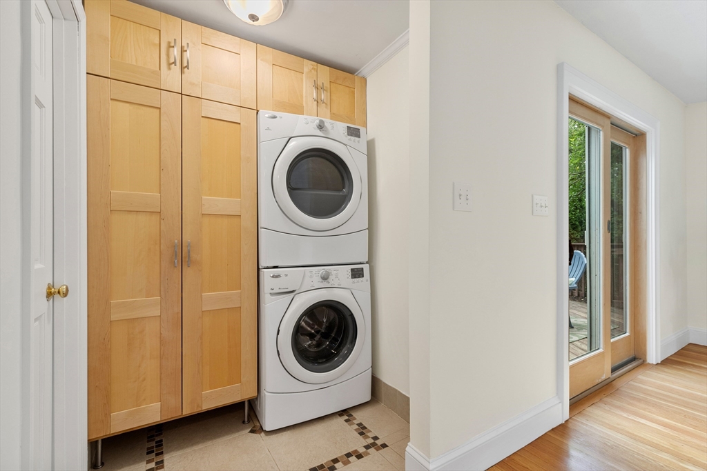 Laundry area with stacked washer and dryer, light wood cabinetry, and a glass door to the deck.