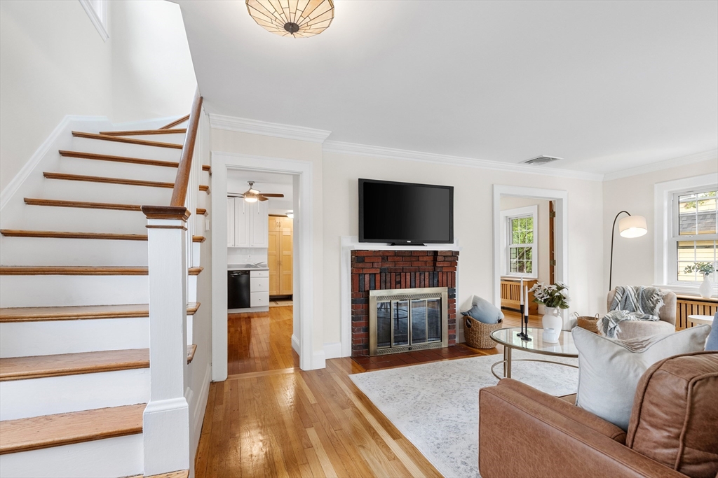 Living room with a brick fireplace, hardwood floors, and a staircase with wood treads.