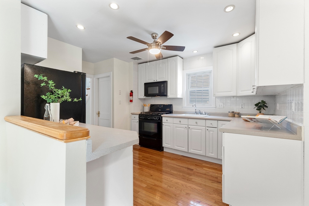 Bright kitchen with white cabinetry, black appliances, hardwood floors, and a wood-trimmed peninsula.