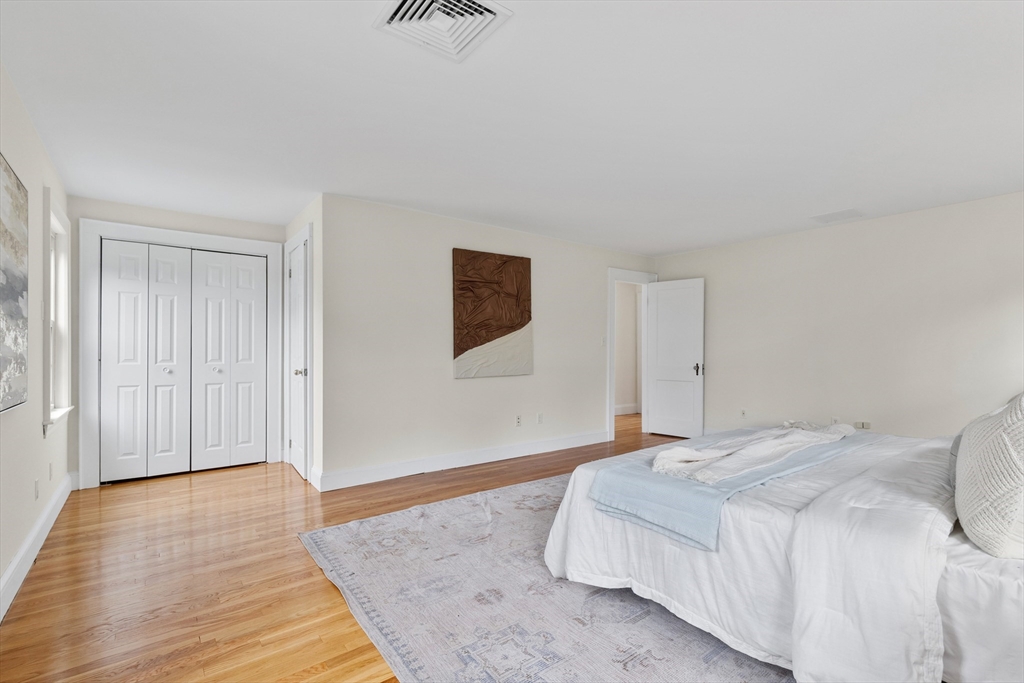 Bedroom with a white bed, pale area rug, hardwood floors, and double closet doors.