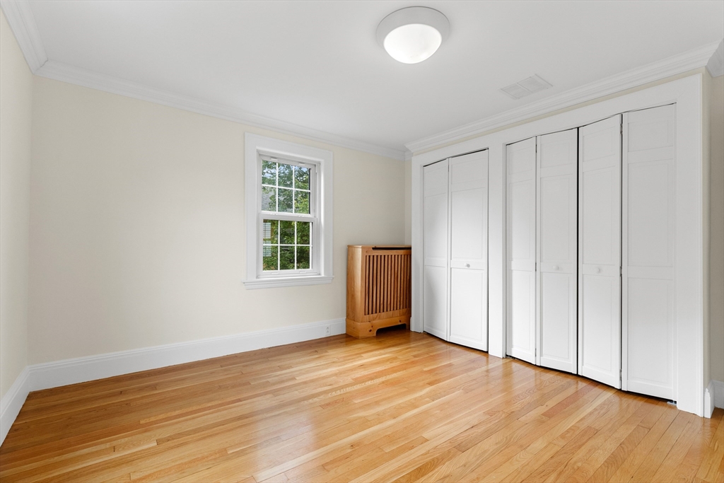 Empty bedroom with hardwood floors, white paneled closets, and a wooden radiator cover.