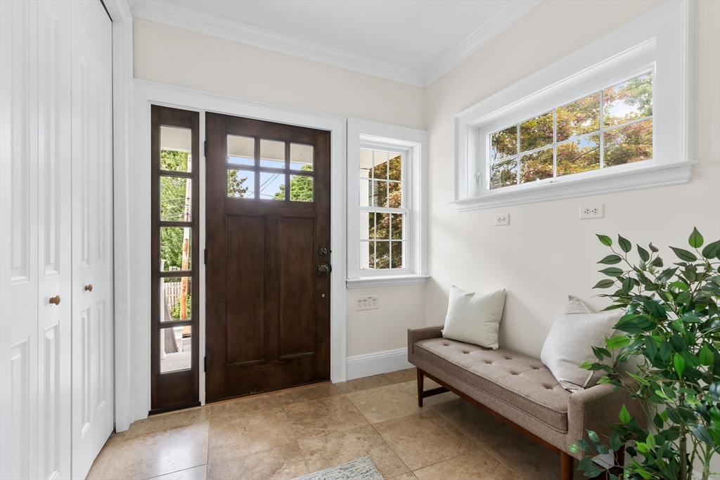 Entry foyer with a dark wood front door, sidelights, tan tile floor, and a cushioned bench beneath large windows.