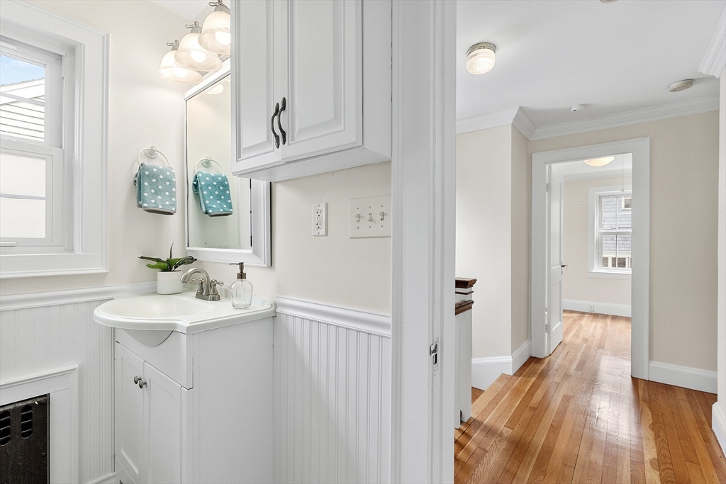 Bright bathroom vanity with beadboard walls beside a hardwood-floored hallway.