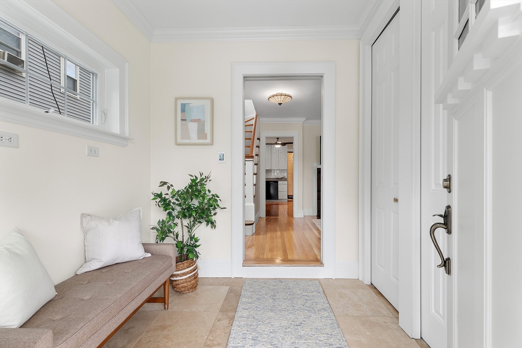 Entry foyer with a white front door, built-in closets, cushioned bench, and view into a hardwood-floored hall.