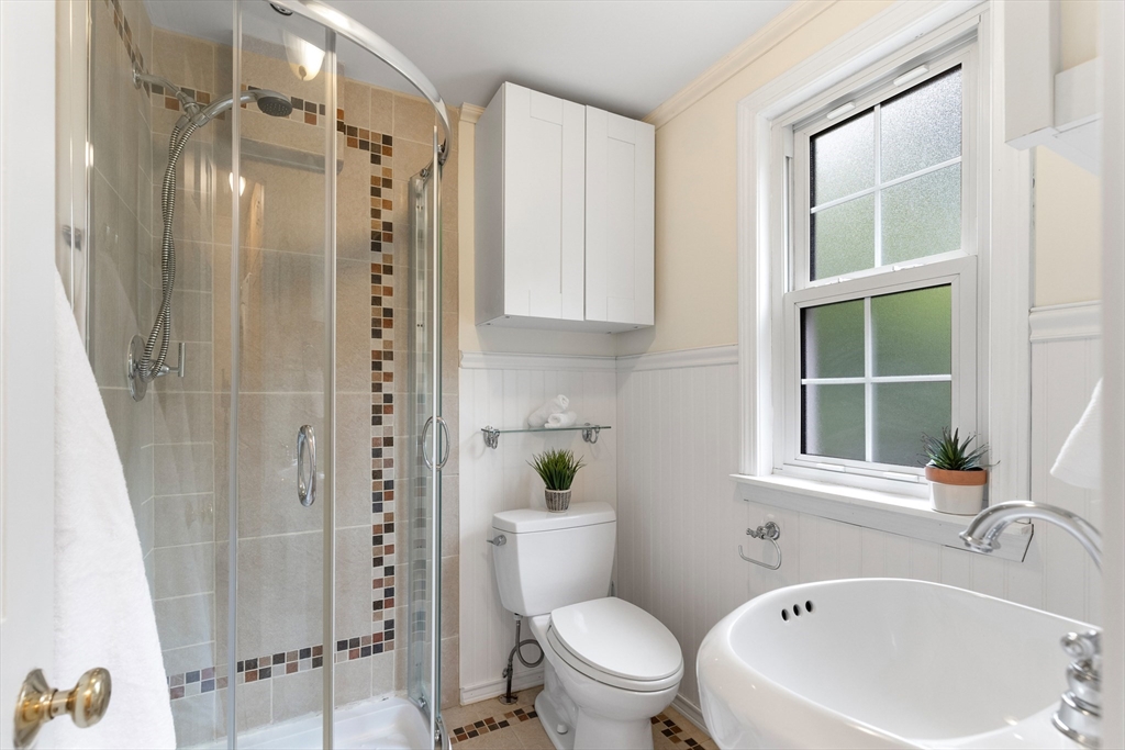 Bright bathroom with a tiled glass shower and large oval sink beside a window.