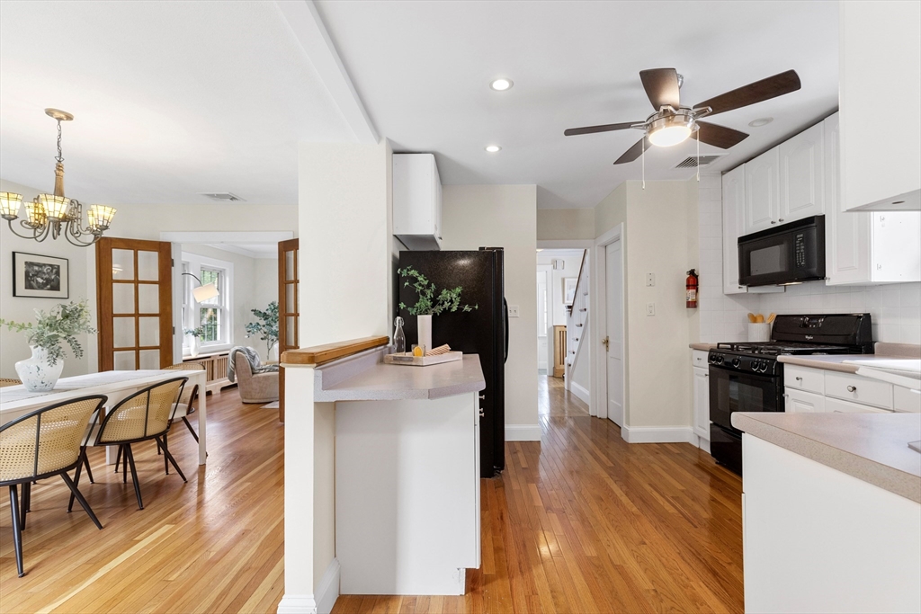 Kitchen with white cabinets, black appliances, a peninsula, and hardwood floors opening to a dining area.