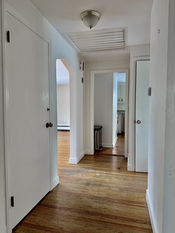 Hallway with hardwood floors, an arched doorway, and a ceiling access panel.