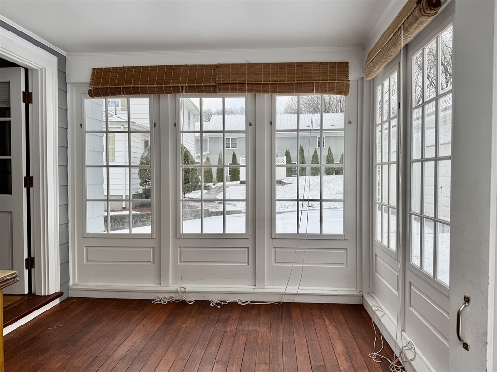 Empty sunroom with tall gridded windows, bamboo shades, and a dark hardwood floor.