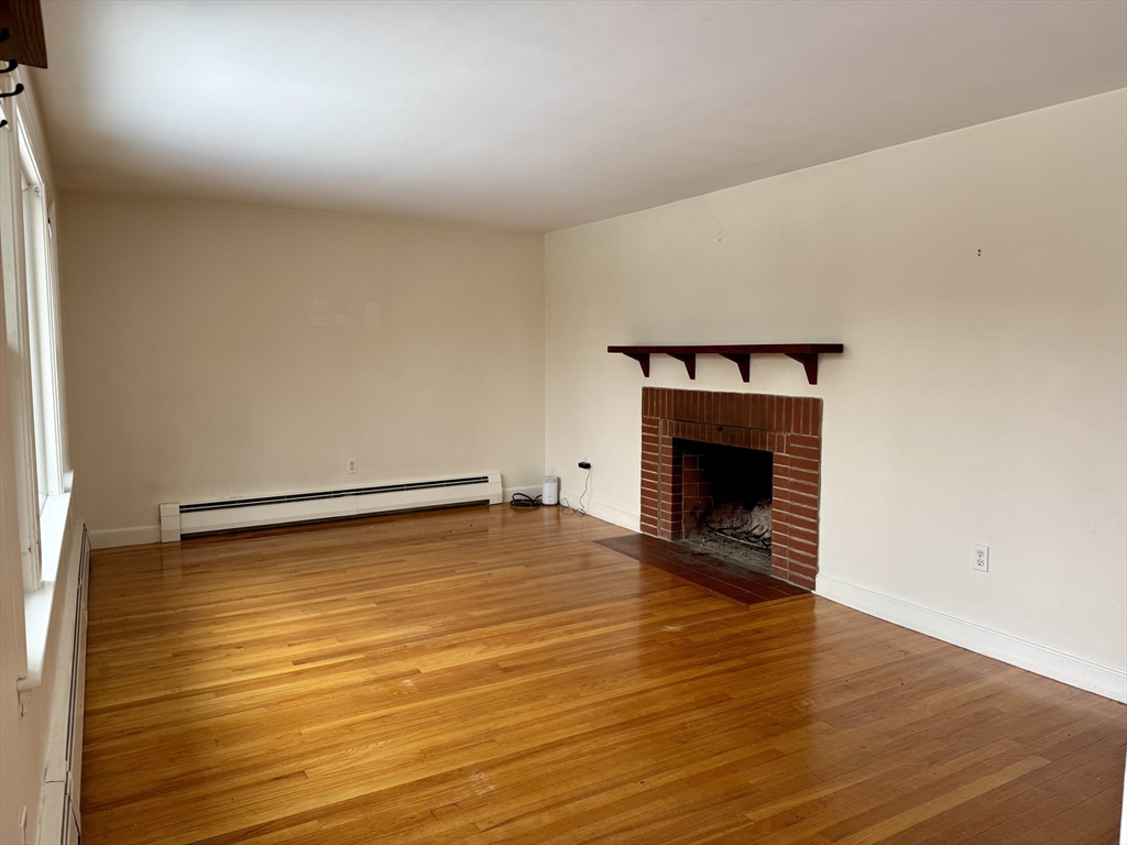 Empty living room with polished hardwood floors and a red brick fireplace.