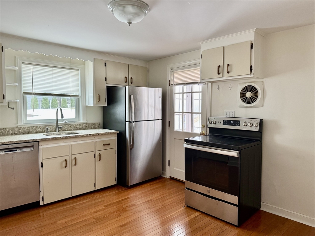 Kitchen with white cabinets, stainless-steel refrigerator, black range, and hardwood floors.