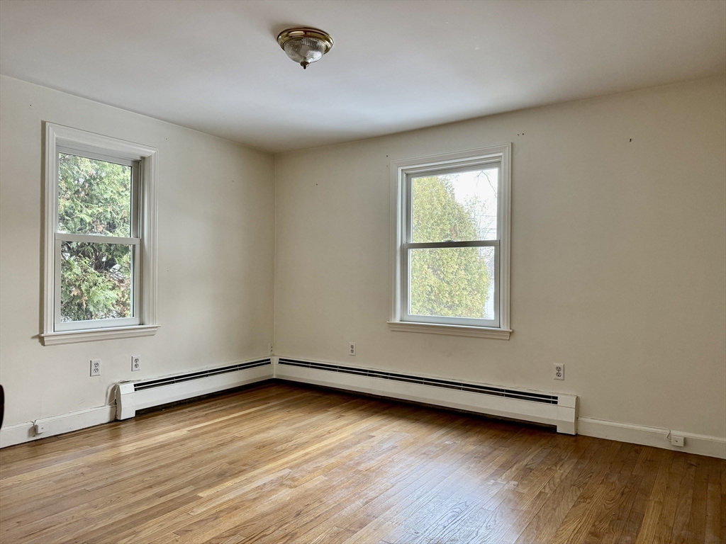 Empty room with hardwood floors, two windows, and baseboard heating.