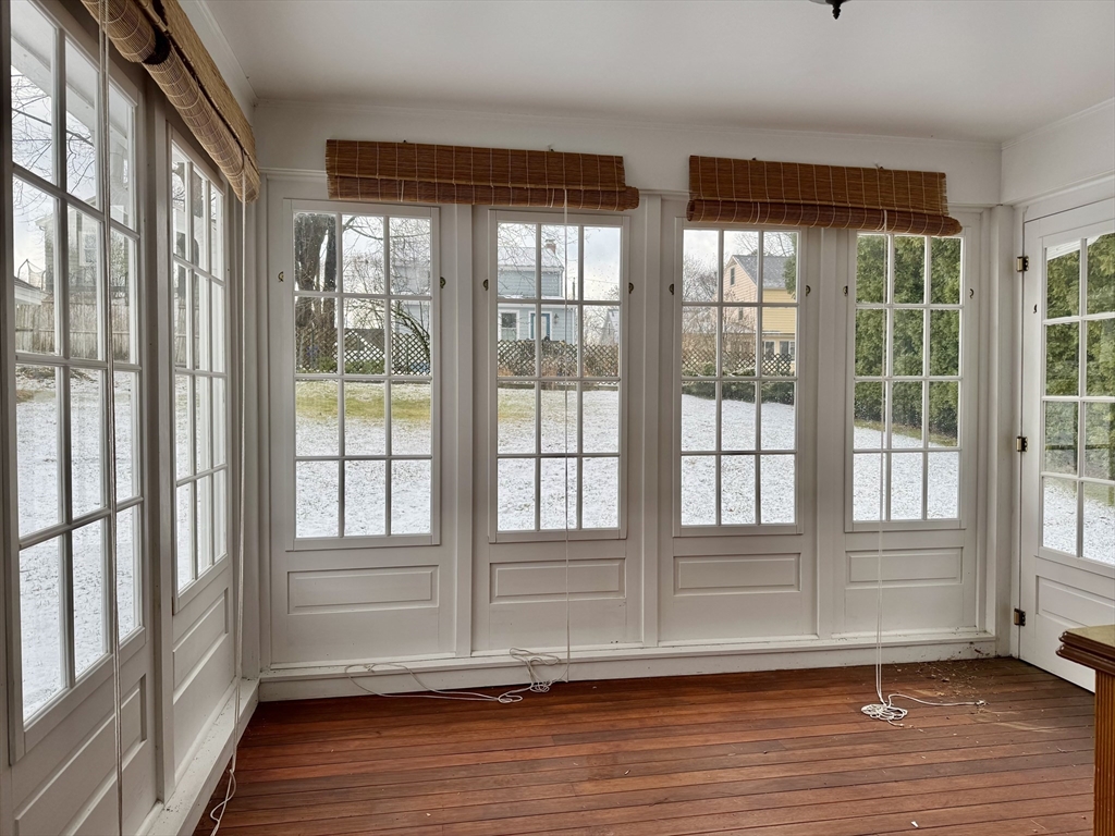 Empty sunroom with tall divided-light windows, bamboo shades, and a wood plank floor.