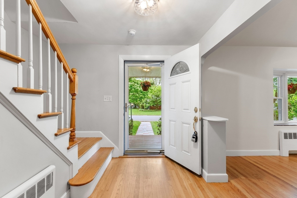 Entry hall with hardwood floors, a staircase, and an open front door facing a green yard.