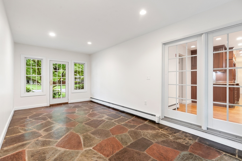 Empty room with a multicolored stone floor, garden-facing windows, and glass doors to a wood-cabinet kitchen.