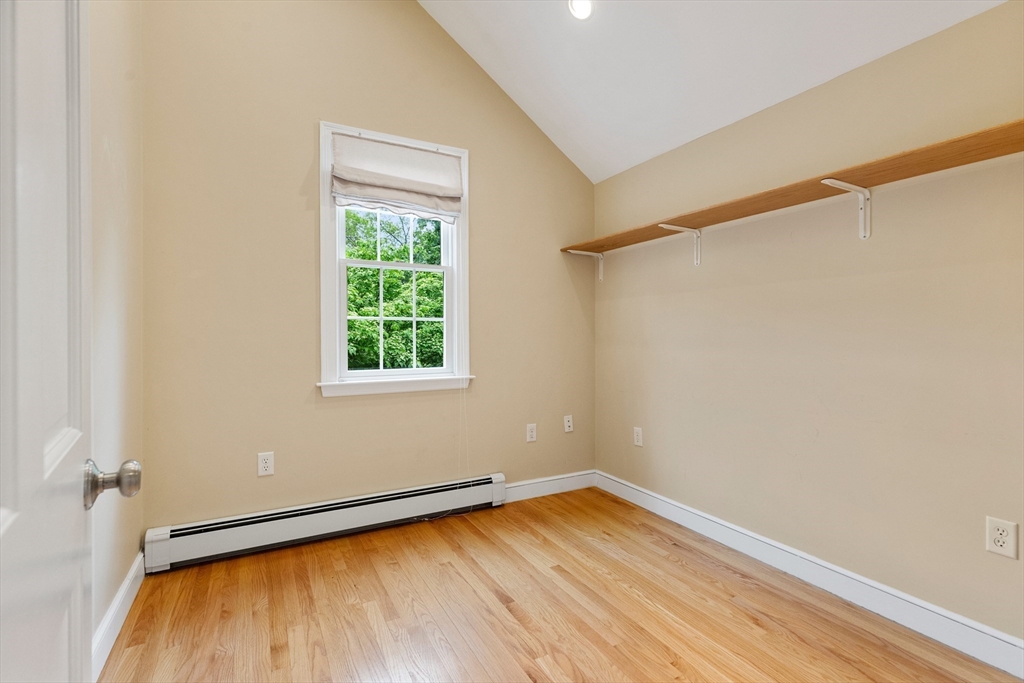 Empty room with hardwood floors, a wall-mounted shelf, and a window overlooking greenery.