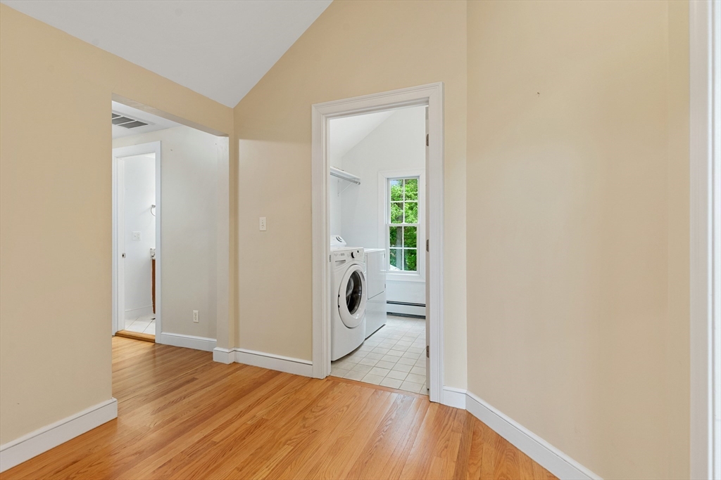 Hallway with hardwood floors and a doorway to a tiled laundry room with a washer and dryer.