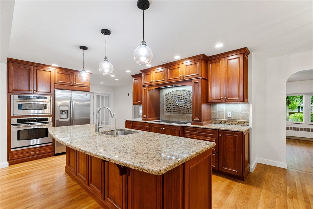 Kitchen with a large granite island, rich wood cabinets, stainless steel appliances, and a mosaic backsplash.