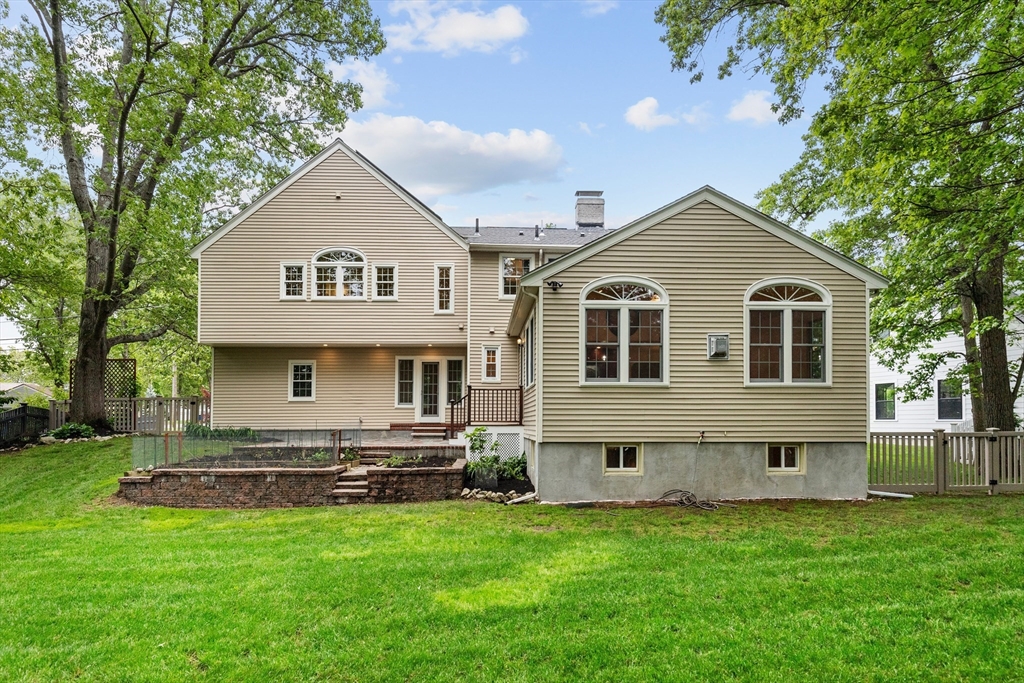 Rear exterior of a beige-sided home with arched windows, stone retaining wall, and broad green lawn.