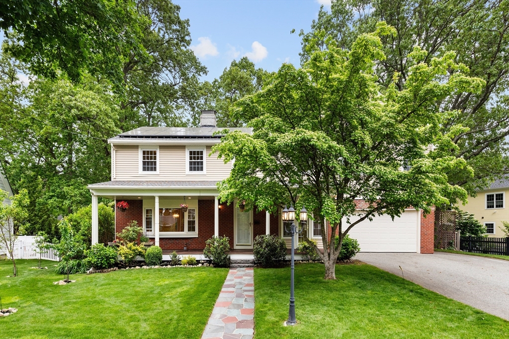 Two-story home with a covered porch, attached garage, and stone walkway through a leafy lawn.