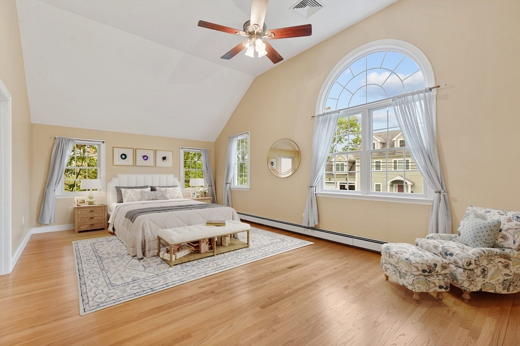 Staged bedroom with a vaulted ceiling, large arched window, and hardwood floors.