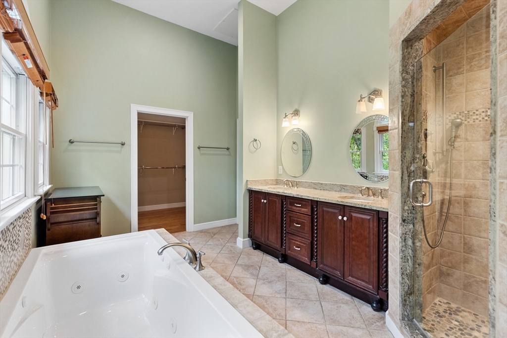 Spacious bathroom with a jetted tub, glass shower, dark wood double vanity, and tall windows.