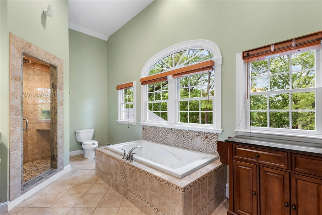 Bathroom with a tiled soaking tub, glass shower, and large arched windows.
