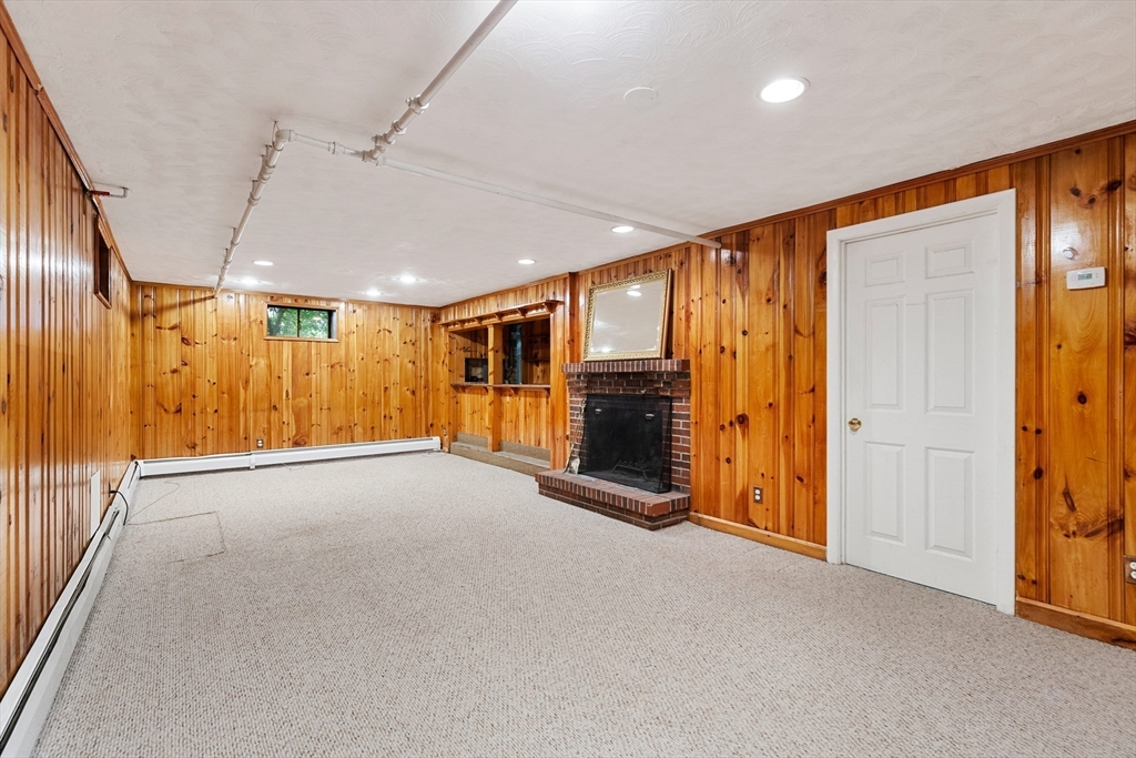 Carpeted basement room with wood-paneled walls and a brick fireplace.
