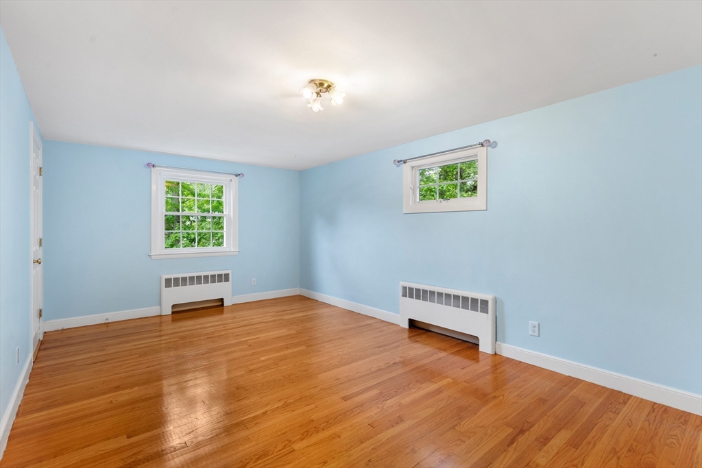 Empty room with light blue walls, polished hardwood floors, two windows, and wall-mounted radiators.
