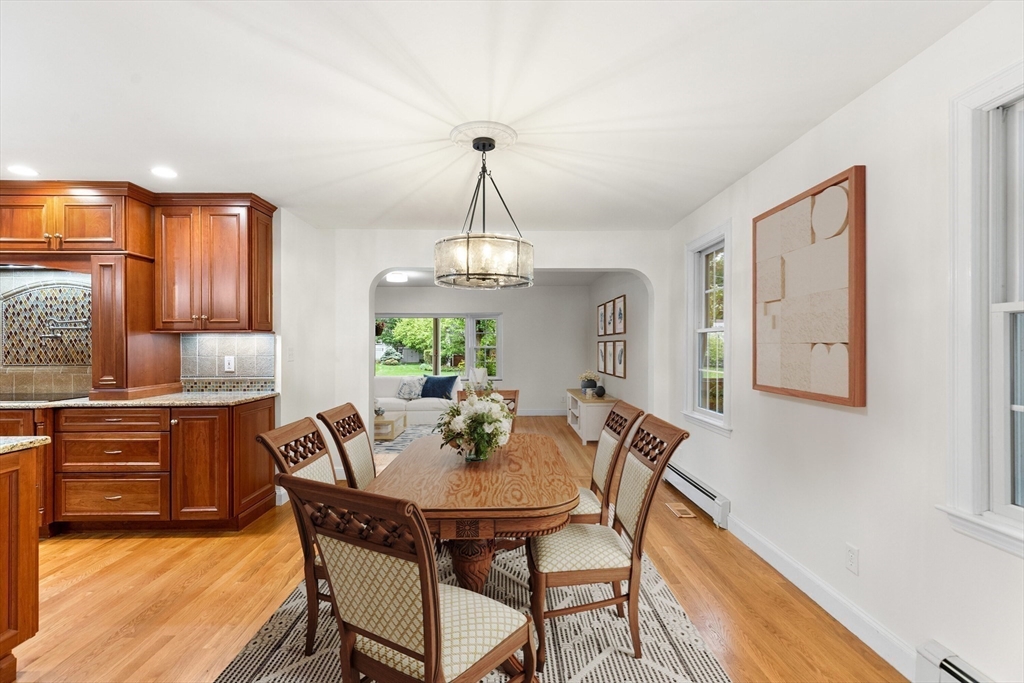 Dining room with a wooden table and upholstered chairs beside a kitchen with rich wood cabinets.