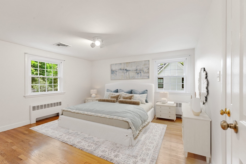 Bright bedroom with a large bed, two windows, and hardwood floors.