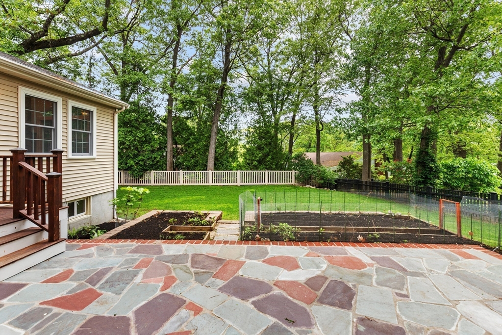 Backyard with a flagstone patio, fenced vegetable garden, and leafy lawn.