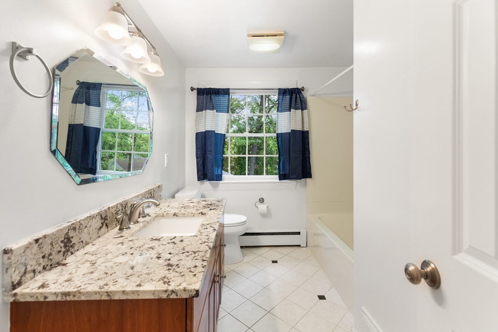 Bathroom with a granite vanity, blue-and-white curtains, and a bathtub.