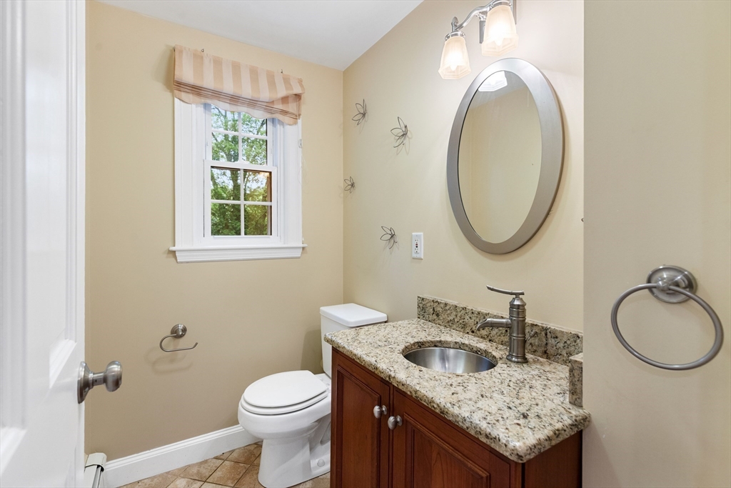 Bathroom with a wood vanity, granite counter, oval mirror, and window with a striped shade.